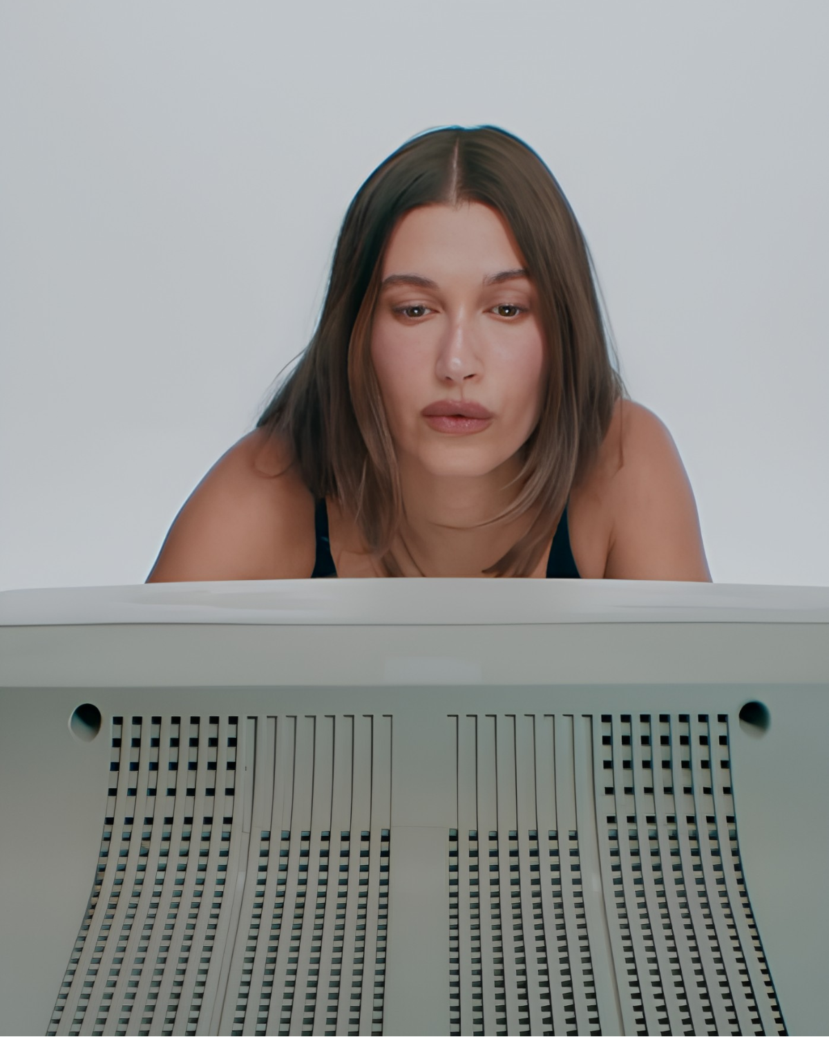 Hailey Bieber leaning over the back of a beige CRT monitor in the Hailey Jean campaign